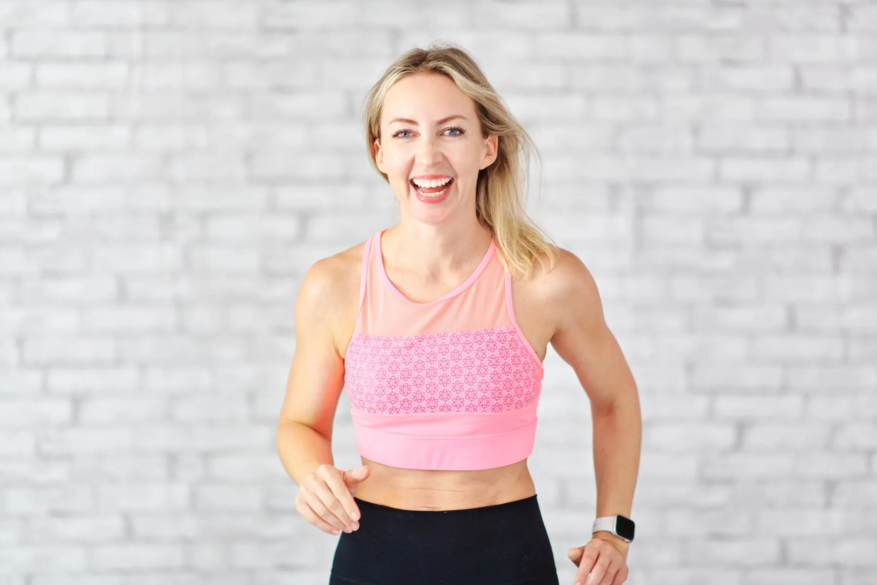 Emma laughing in a pink sports top in front of a white brick wall