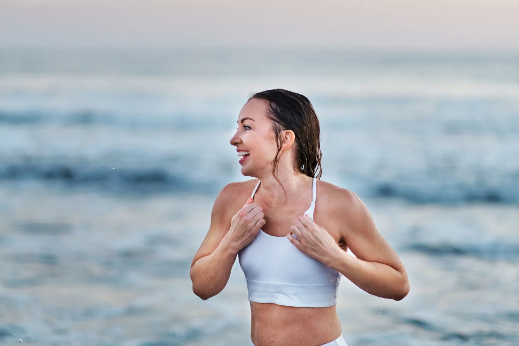 Emma smiling at the water's edge in a white sports top