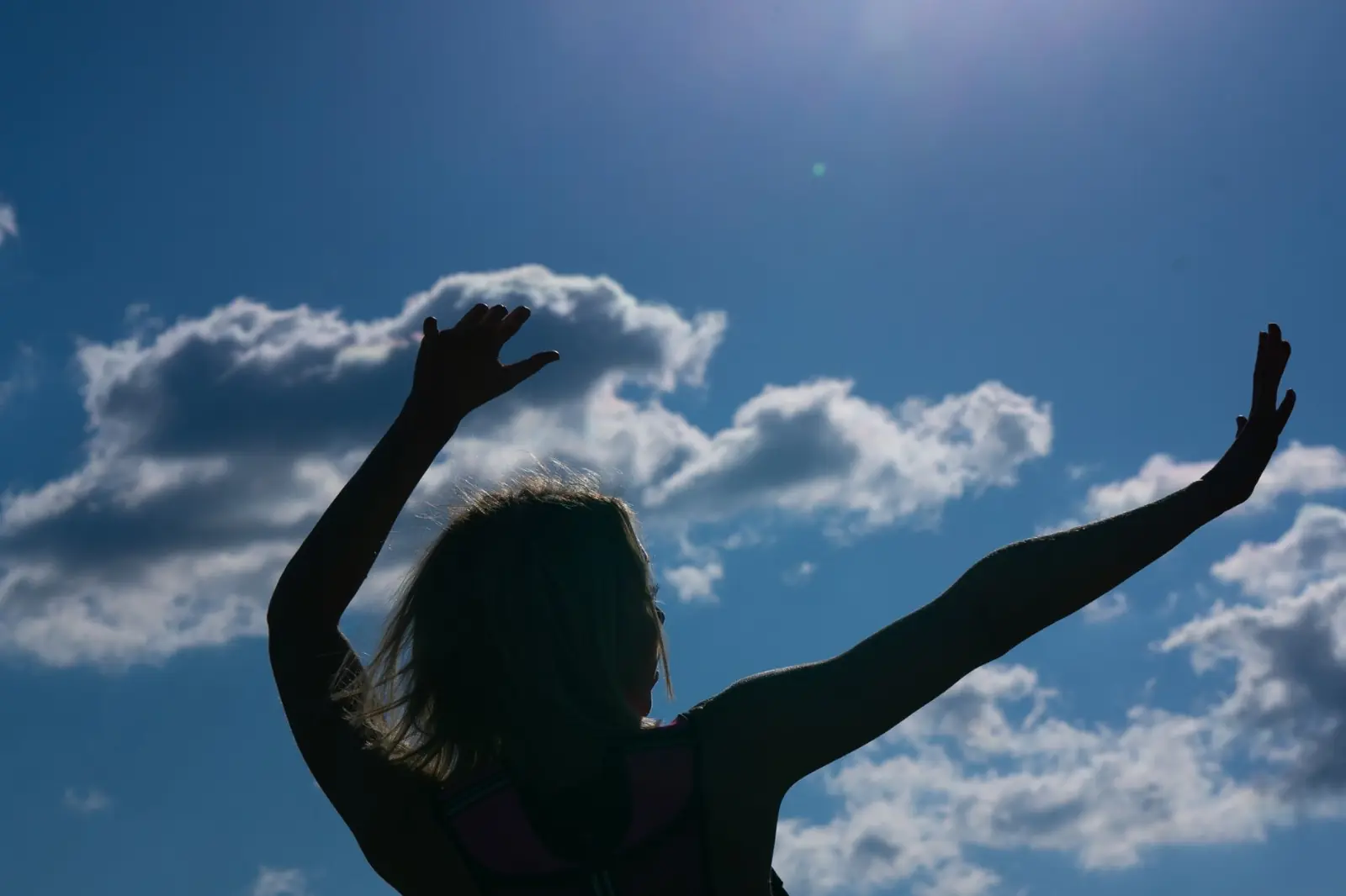 Emma in silhouette against a sunny blue sky, arms raised