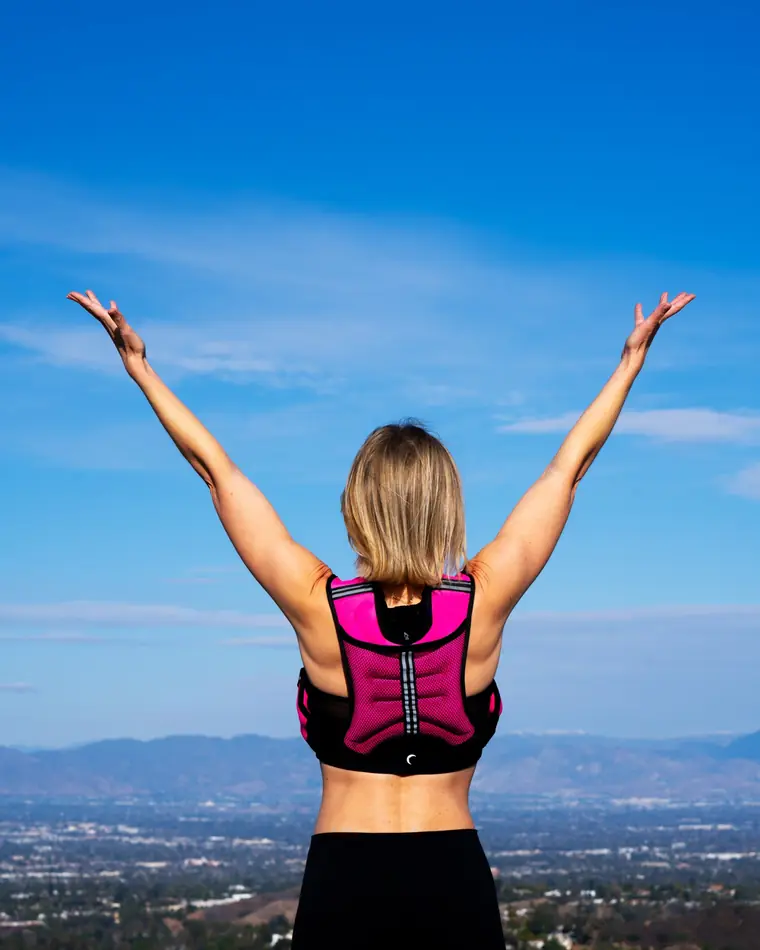 Emma from behind on a hilltop, arms raised to the sky above the valley