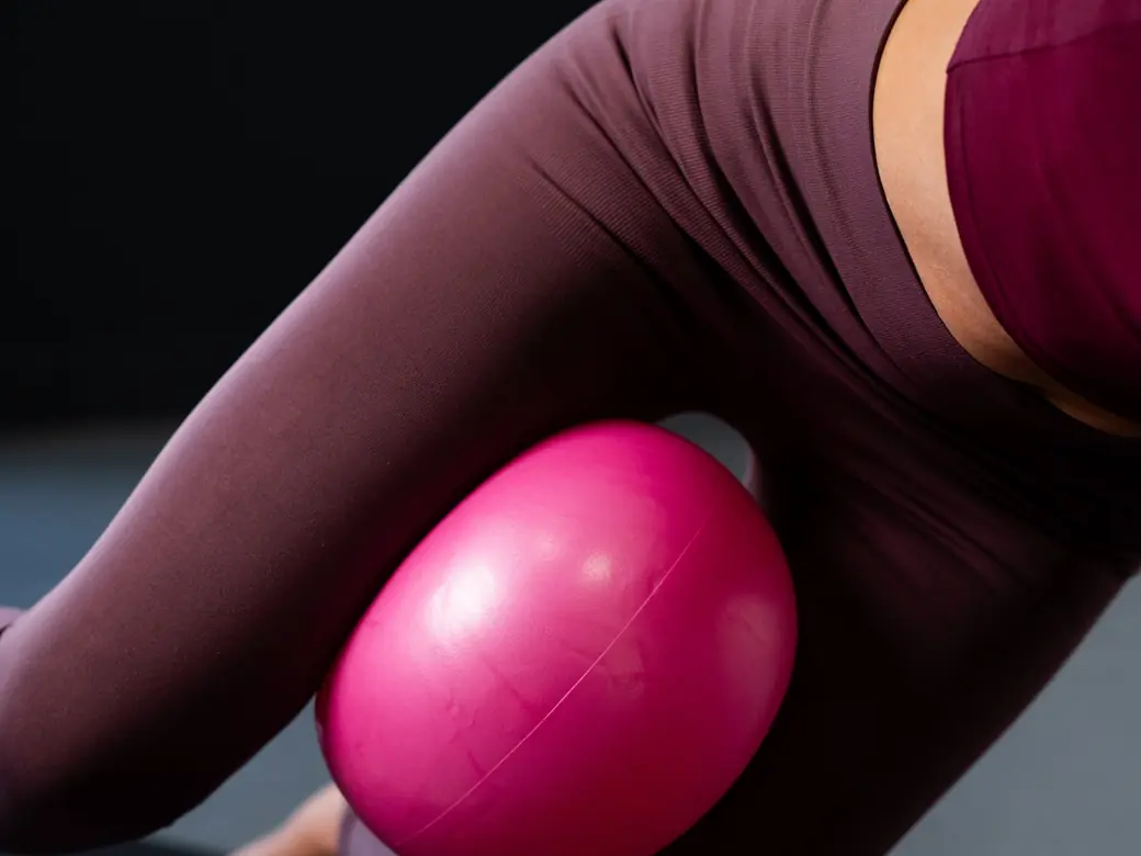 Close-up of a pink Pilates ball squeezed between Emma's knees