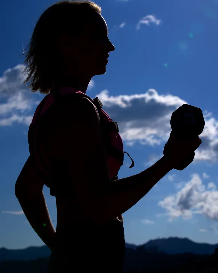 Emma in silhouette against a blue sky, curling a dumbbell