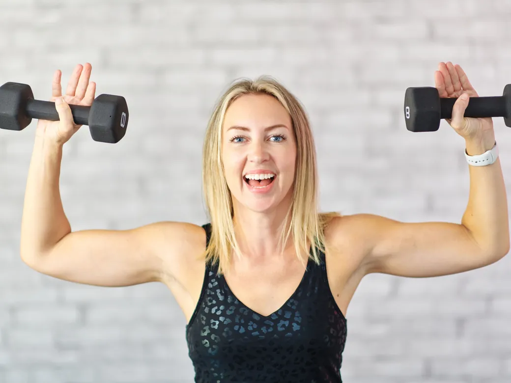 Emma pressing two dumbbells overhead, laughing